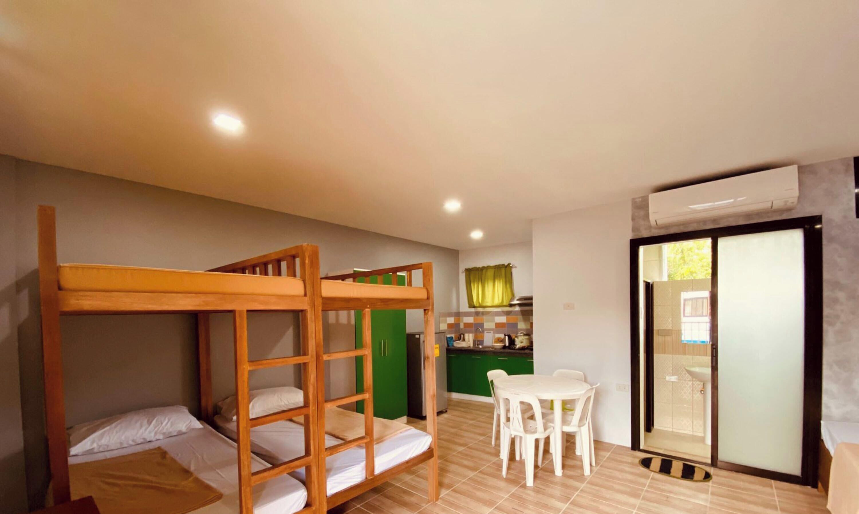 A room with bunk beds, a dining table with chairs, a kitchen area, and a sliding glass door.