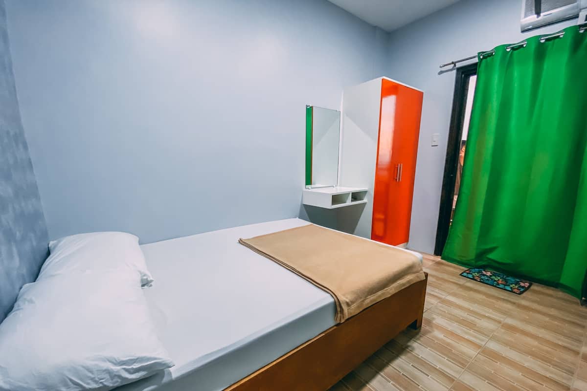 A room with a bed, a wardrobe, a mirror, and a green curtain.