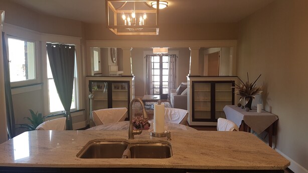 A kitchen with a marble countertop, two sinks, a chandelier, and a view of a living room with a sofa and a window.