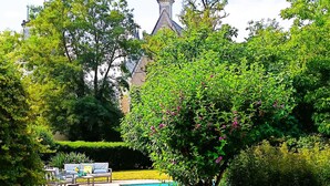 A swimming pool surrounded by lush greenery and a building with a prominent tower in the background.