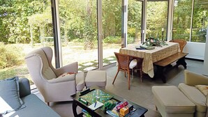 A sunlit room with a large sliding glass door leading to a garden, furnished with a sofa, a table, and a chessboard.