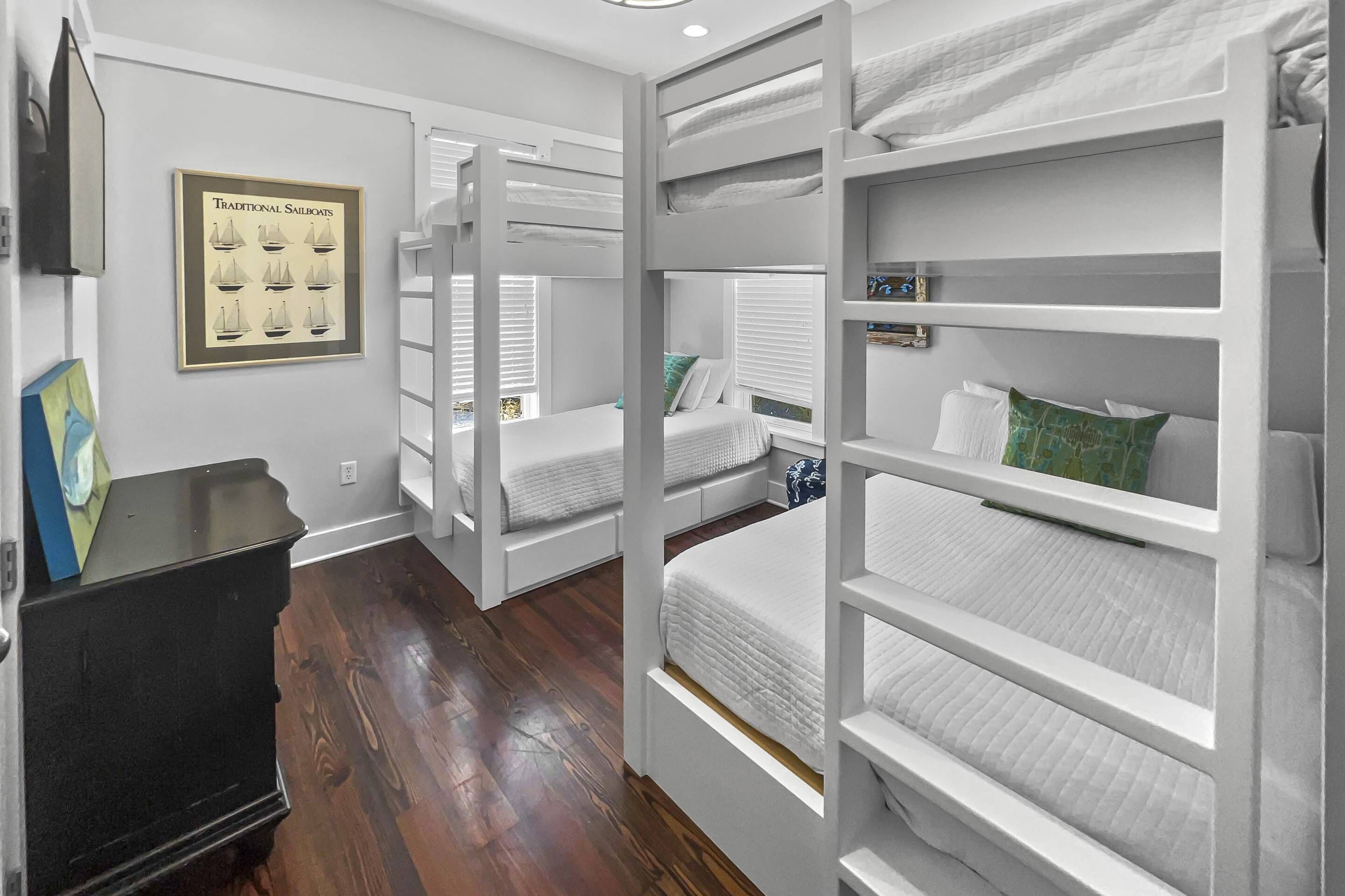 A room with bunk beds, a framed picture of sailboats, and a black dresser.