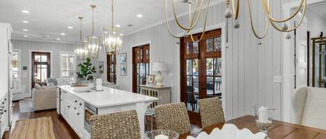 A spacious kitchen with a large island, pendant lighting, and a dining area with a wooden table and woven chairs.