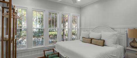 A bedroom with a large bed, a ceiling fan, and a window with blinds.