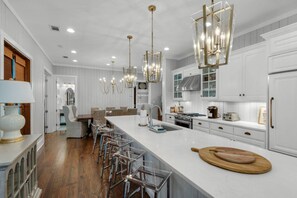 Una cocina moderna con armarios blancos, una isla grande y una zona de comedor con sillas transparentes.