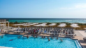 Uma área de piscina com espreguiçadeiras e guarda-sóis, com vista para o oceano.