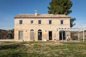 A two-story brick building with a tiled roof, a wooden pergola, and a grassy lawn.