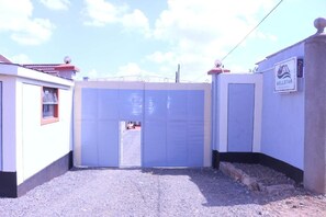 A gated entrance with a blue gate, a WELLSTAR sign, and a building with a red roof. - Well Star Guest House (Nairobi)