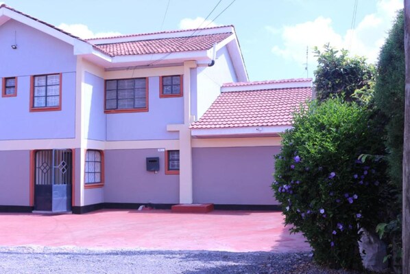 A two-story building with a red-tiled roof, a gated entrance, and a small garden area with purple flowers. - Well Star Guest House (Nairobi)