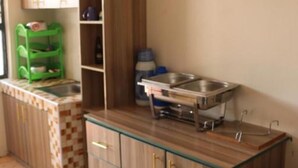 Une cuisine de taille réduite, avec des meubles de rangement en bois, un évier et une étagère verte.