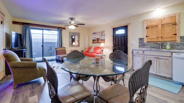 A dining area with a glass table surrounded by wicker chairs, a red sofa, and a television in the background. - Fort Worth Home w/ Patio: 5 Mi to Dtwn! (Fort Worth)