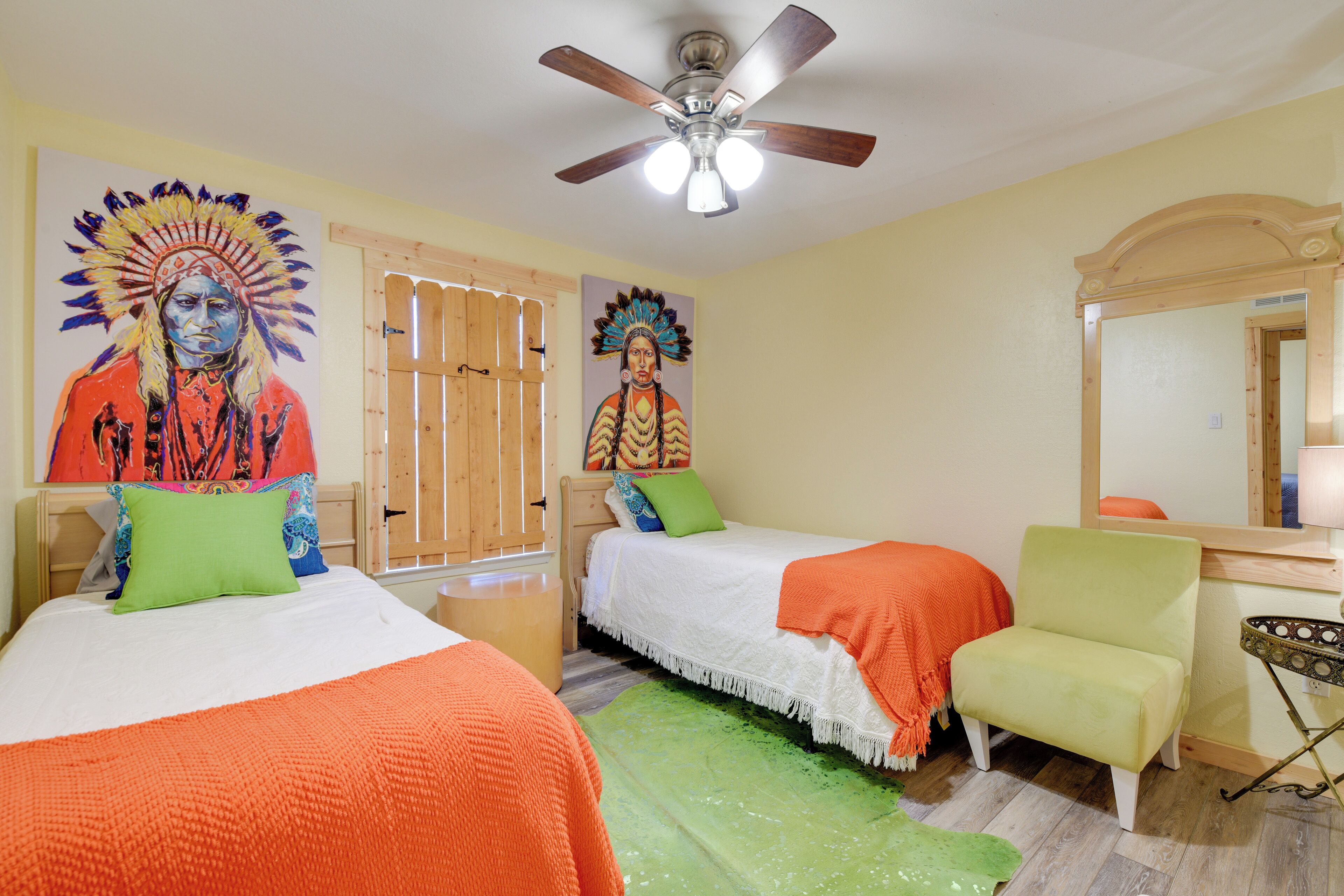 A bedroom with two beds, a green rug, a ceiling fan, and a wooden door.