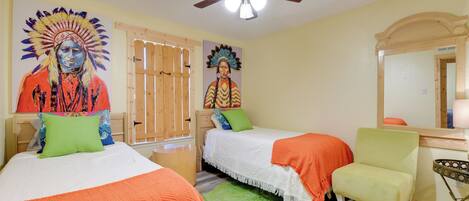 A bedroom with two beds, a green rug, a ceiling fan, and a wooden door.