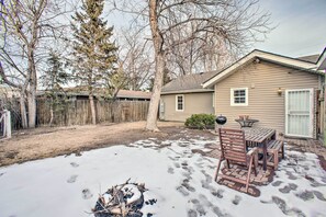 A backyard with a wooden table and chairs, a fire pit, and a snow-covered ground.