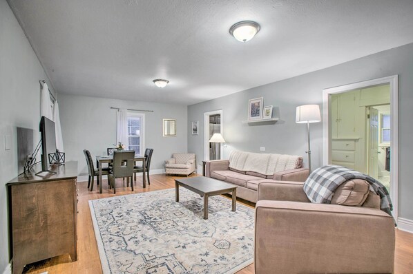 A living room with a sofa, armchair, coffee table, and dining table.