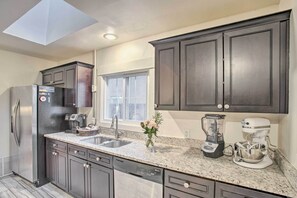 A modern kitchen with dark cabinets, a stainless steel refrigerator, a built-in dishwasher, a coffee maker, and a stand mixer. - Walkable Neighborhood: Family Home in Wheat Ridge (Wheat Ridge)