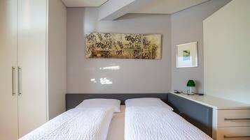 Quarto com duas camas de solteiro, uma pintura abstrata grande, uma fotografia emoldurada, uma mesa de cabeceira com luminária e um guarda-roupa.