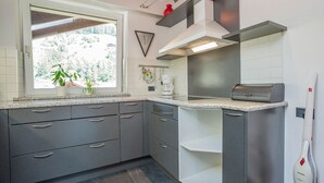Une cuisine moderne avec des meubles gris, une fenêtre ornée de plantes, une machine à café et un four encastré.