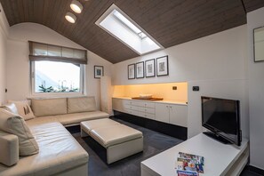 Una sala de estar moderna con sofá, reposapiés, televisor y tragaluz.