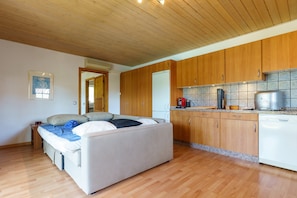A room with a bed, wooden cabinets, a kitchen area, and a tiled backsplash.