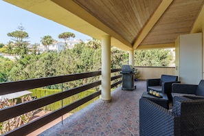 A covered outdoor area with a patio, seating, and a view of the surrounding greenery and buildings.