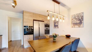Een moderne keuken met houten kastjes, een eettafel met stoelen en een hangende lamp.