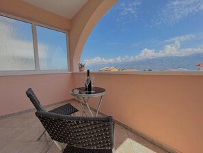 A balcony with a wicker chair, a small round table, and a potted plant.