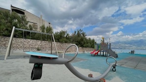An outdoor playground with a seesaw, a slide, and a climbing structure. - Apartment Nico (Razanac)
