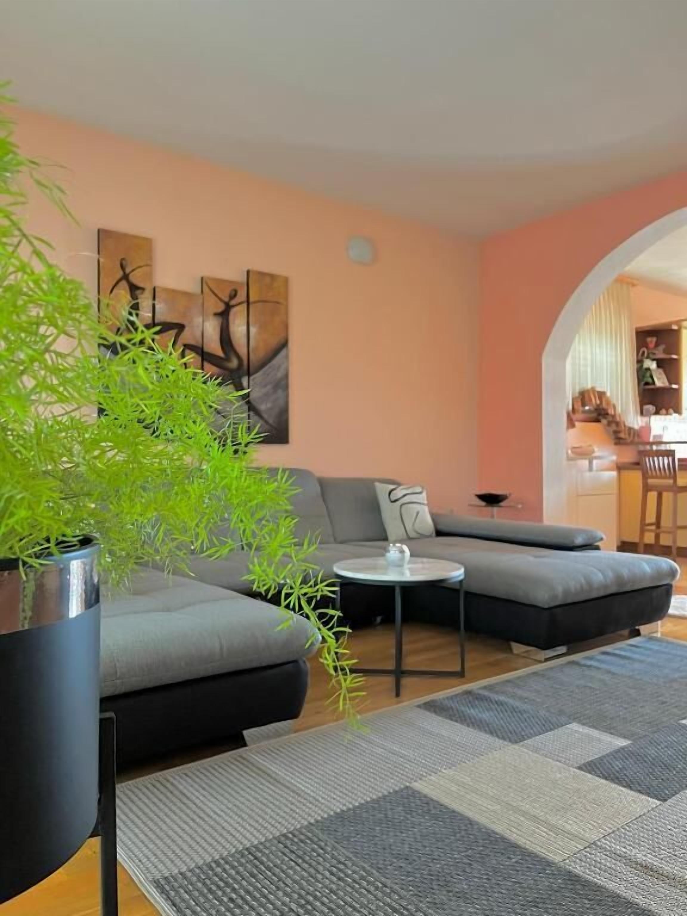 Un salon moderne avec un canapé d’angle gris, une petite table basse ronde et une plante en pot.