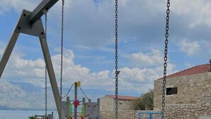 A playground with swings and a slide, set against a stone wall and a clear sky. - Apartment Nico (Razanac)