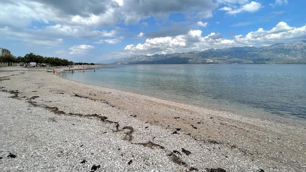 A pebbled beach with a clear view of distant mountains and a partly cloudy sky. - Apartment Nico (Razanac)