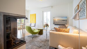 En moderne stue med pejs, lænestol i grøn farve, hvid sofa og et stort fladskærms-tv.