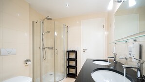 A modern bathroom with a glass-enclosed shower, two sinks, and a large mirror. - Villa Estrelia, App. 6 (Heringsdorf)