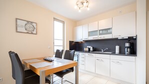 A modern kitchen with white cabinets, a wooden dining table, and a framed watch on the wall. - Villa Estrelia, App. 6 (Heringsdorf)