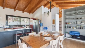A modern kitchen with a wooden ceiling, a dining area with a wooden table and white chairs, and a built-in shelving unit with glassware. - Studio 'Guest House - Loft Cim Apartments 3' with Mountain Views, Wi-Fi, and Air Conditioning (Olivella)