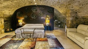 A bedroom with a stone ceiling, a bed with a metal frame, a beige sofa, and a rug with a geometric pattern. - Holiday Home "Mas Renart" with Mountain View, Pool, Wi-Fi, Garden & Terrace (Mollet de peralada)