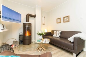 A living room with a modern fireplace, a brown leather sofa, a glass coffee table, and a framed picture on the wall. - Villa Limora, App. 03 (Heringsdorf)