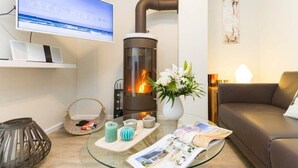 Ein gemütliches Wohnzimmer mit Glastisch, Sofa, Fernseher, Kamin und einer Blumenvase.