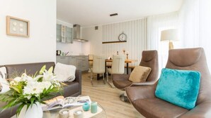 Ein modernes Wohnzimmer mit einer Couch, Sesseln, einem Couchtisch und einem Essbereich im Hintergrund.