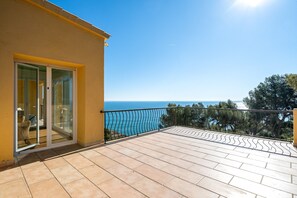 Un balcon offrant une vue dégagée sur la mer, une porte vitrée donnant sur l’intérieur et un sol carrelé.