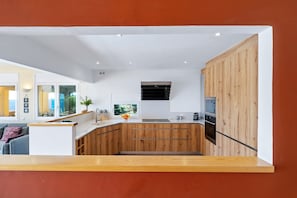 A modern kitchen with wooden cabinets, a built-in oven, and a window overlooking a garden. - Villa 'The Beauty of Cala Tamarit' with Sea View, Pool, Wi-Fi and Garden (Tarragona)