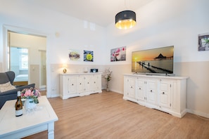 Un salon avec un canapé, une table basse sur laquelle se trouvent une bouteille et des verres, un téléviseur posé sur un meuble, et des œuvres d’art accrochées aux murs.