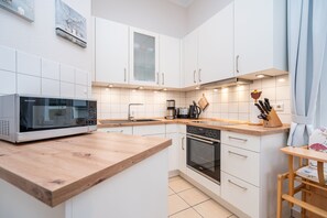 Een moderne keuken met witte kastjes, een magnetron, een koffiezetapparaat en een houten aanrecht.