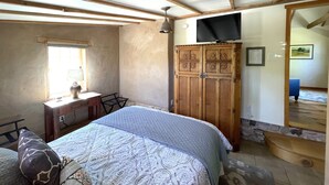 A bedroom with a bed, a wooden wardrobe, a desk, and a television.
