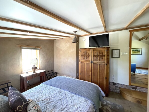 A bedroom with a bed, a wooden wardrobe, a desk, and a television.