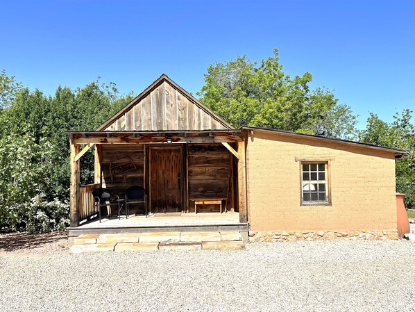 Un edificio rústico de madera con un porche, un pequeño añadido de ladrillo y una ventana.