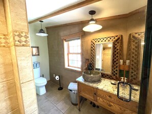A bathroom with a toilet, sink, mirror, and a window.