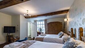 Hotelkamer met twee bedden, een televisie, houten balken, een kledingkast en een raam met gordijnen.