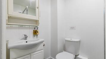 Un baño pequeño y limpio con lavamanos, espejo e inodoro blancos.