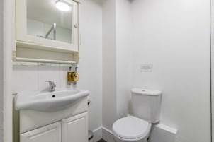 Un baño pequeño y limpio con lavamanos, espejo e inodoro blancos.